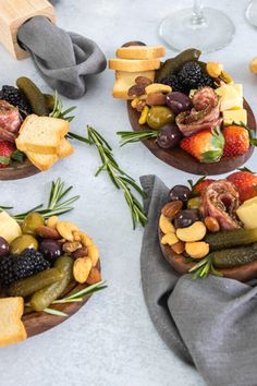 four wooden bowls filled with assorted fruits and veggies next to wine glasses