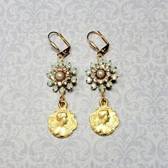 Pretty 10k gold plated maiden charms dangle beneath embellished vintage brass connectors. The connectors are set with glass rhinestones in chrysolite opal color (light seafoam green) and clear crystal with a glass pearl center. These earrings are 2-1/4 inches long including the leverback earwires. Make a glamorous statement with this elegant pair of earrings✨ ✨ Note: I do my best to take accurate photos. Please be aware that colors and brightness can vary slightly between different monitors and Antique Gold Jeweled Earrings, Vintage Jeweled Drop Earrings, Nickel Free Gold Earrings For Vintage Collection, Handmade Gold Earrings For Vintage Collection, Vintage Collection Dangle Jewelry With Matching Earrings, Victorian Jeweled Gold Earrings, Vintage Gold Crystal Earrings For Pierced Ears, Brass Jeweled Drop Earrings, Antique Gold Earrings With Vintage Charm