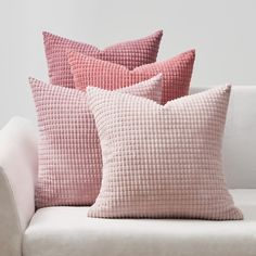 three pink pillows sitting on top of a white couch