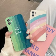 two people holding up their cell phones in front of them, one has a rainbow case and the other has a smiley face on it