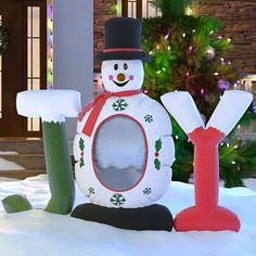 an inflatable snowman sitting next to a christmas tree