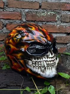 a motorcycle helmet with flames painted on it sitting in front of a brick wall and ivy