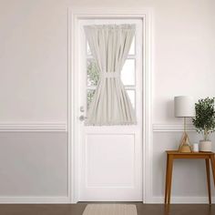 a white door with curtains and a rug on the floor in front of it next to a table