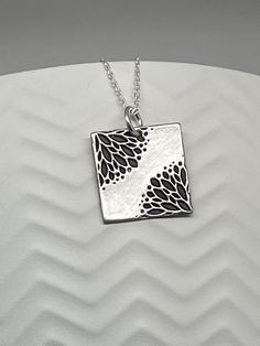 This Silver Floral Square Necklace is handmade using .950 sterling silver. It has been cut from sterling silver precious metal clay, textured, fired and oxidized. The pendant hangs from a sterling silver diamond cut cable chain. This sterling silver pendant features an embossed lovely Art Deco style floral textured print pattern Pendant size: approximately 5/8 x 5/8 inches Chain length: adjustable at 16 and 18 inches can also be customized to whatever length needed The necklace is sent in a gift Elegant Stamped Flower Pendant Necklace, Elegant Stamped Flower Pendant Necklaces, Unique Etched Sterling Silver Necklace, Etched Sterling Silver Necklaces, Silver Etched Sterling Silver Necklace, Antique Silver Etched Sterling Silver Necklace, Silver Etched Necklace With Flower Pendant, Artisan Silver Etched Necklace, Sterling Silver Etched Necklace For Gift