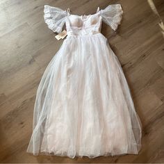 a white dress with ruffles on the shoulders and neckline is laying on a wooden floor