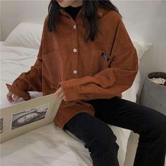 a woman is sitting on a bed and holding an open book in her hand while wearing black pants