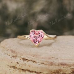 a pink heart shaped ring sitting on top of a rock