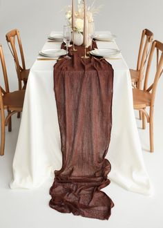 the table is set with white and brown linens, gold place settings and candles