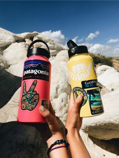 someone holding up two water bottles in front of some rocks