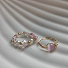 two rings with pink and white beads sitting on top of a plate next to each other