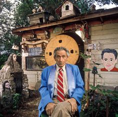 a man in a blue jacket and red tie sitting on a chair next to a house