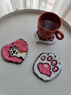 three coasters with pink and white designs on them sitting next to a coffee cup