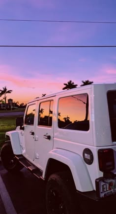 a white jeep parked in a parking lot with the sun setting behind it and palm trees