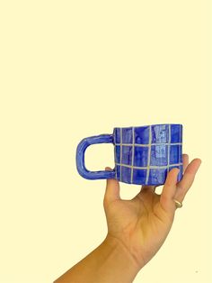 a hand holding a blue coffee mug in front of a white background with squares on it