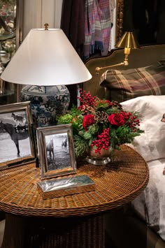 a wicker table topped with a vase filled with flowers next to a lamp and pictures