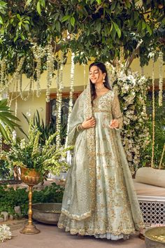 a woman standing under a tree wearing a green lehenga with gold and white flowers