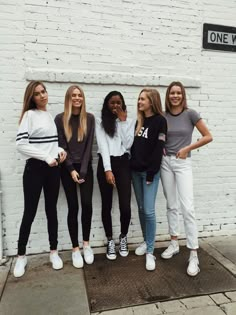 four girls are standing in front of a white brick wall and posing for the camera