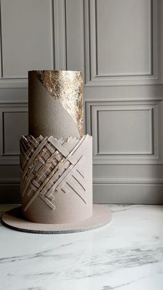 a three - tiered cake with gold leaf decoration on top sits on a marble table