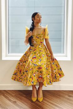 a woman standing in front of a window wearing a yellow dress with flowers on it