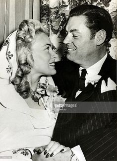 black and white photograph of two people sitting next to each other, one kissing the other