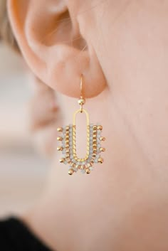 a close up of a person wearing earring with gold and white beads on it