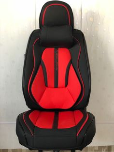 a red and black car seat sitting on top of a wooden floor next to a wall