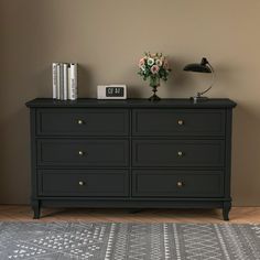 a black dresser sitting on top of a wooden floor next to a lamp and flowers