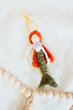 a little mermaid keychain is sitting on a white surface with beads around it