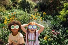 two young children with sun glasses on their faces in the middle of a flower garden