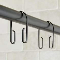 three hooks are hanging on the side of a white brick wall with black metal bars