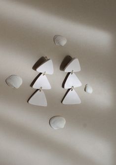 three pairs of white earrings with seashells hanging from them on a wall in the sunlight