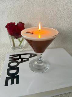 a drink in a martini glass on top of a book with a lit candle next to it