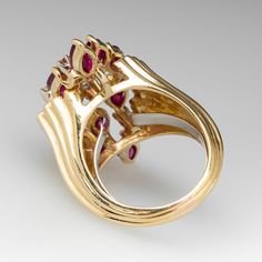 This vintage cluster ring features twelve (12) two-prong set, marquise cut rubies that are accented with seven (7) round brilliant cut diamonds. The shoulders feature a graduated, tiered design. The ring measures 36.4mm at the top, rises 13.6mm above the finger, tapering to 4.3mm wide and 1.9mm thick at the base of the shank. It is currently a size 8.25 with a spring ring insert. Formal Ruby Ring With Diamond Accents In Cluster Shape, Formal Cluster Ruby Ring With Diamond Accents, Marquise Multi-stone Cluster Ring For Formal Occasions, Formal Marquise Multi-stone Cluster Ring, Formal Marquise Cluster Ring With Multi-stone, Formal Marquise Cut Gemstone Cluster Ring, Formal Oval Ruby Ring With Single Cut Diamonds, Formal Cluster Ruby Ring, Vintage Ruby Cluster Ring For Formal Occasions