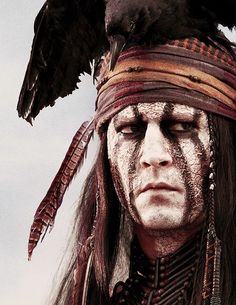 a man with white paint on his face and headdress has a crow perched on his shoulder