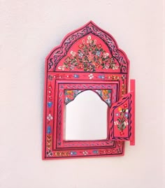 a mirror mounted to the side of a white wall next to a red frame with flowers on it