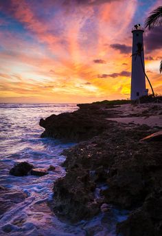 a light house sitting on top of a rocky beach next to the ocean at sunset