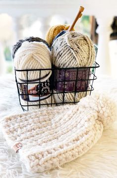 two balls of yarn sit in a basket on a white blanket next to a crochet dishcloth