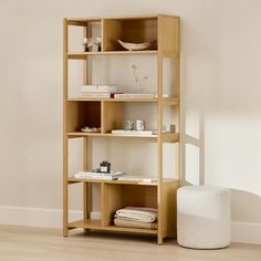 a wooden shelf with books on top of it next to a white stool and wall