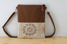 Bolso de lona en color marrón, combinado con tela estampada con motivos de ganchillo. Esta hecho con tela de alta calidad. El asa está hecha con la misma lona, acolchada para darle mayor resistencia, con un regulador para que puedas ajustarla  ala medidas que quieras, tanto cruzado como para llevar en el hombro. No tiene bolsillos, el compartimento principal se cierra con una cremallera que acaba en un tirador de cuero marrón. Forrado con tela acolchada. Muy practico para llevar a diario y muy c Brown Mobile Phone Bag For Fall, Brown Canvas Bag For Daily Use In Fall, Brown Canvas Bag For Fall, Casual Brown Clutch Shoulder Bag, Handmade Beige Crossbody Satchel, Brown Crochet Tote Bag For Mobile Phone, Handmade Fall Shoulder Bag, Brown Crochet Shoulder Bag, Handmade Brown Canvas Bag Casual Style