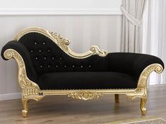 a black and gold couch sitting on top of a hard wood floor next to a window