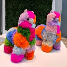 two colorful stuffed llamas sitting on top of a white table next to each other