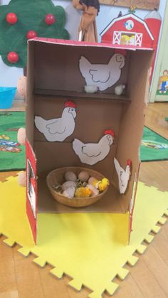 an open cardboard box with chickens and eggs in it on the floor next to other toys