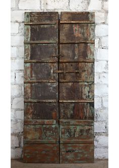 an old wooden cabinet with rusted paint on the doors and drawers, against a white brick wall