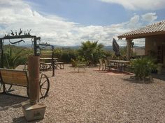 an old fashioned wagon sitting in the middle of a gravel lot with tables and chairs around it