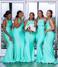 a group of women standing next to each other in front of a large window wearing green dresses