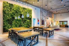 an indoor dining area with tables and chairs in front of a wall covered with green plants