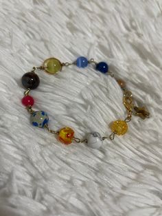 a bracelet with multicolored glass beads and gold tone chain on white furnishing