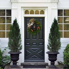 a black front door with two large planters and a wreath on it's side