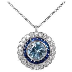 Exquisite and captivating, this Art Deco-inspired pendant is a true masterpiece. The centerpiece of this enchanting creation is an approximately 1.70-carat round aquamarine, radiating a tranquil blue hue. Embracing the aquamarine is a double halo of meticulously arranged calibre-cut sapphires, forming a celestial backdrop. Adding to its allure, a cluster of old European cut diamonds dances around the pendant, each diamond reflecting light with exceptional brilliance. The craftsmanship of this pendant is unparalleled, as it is meticulously handcrafted in platinum, a noble metal known for its durability and timeless elegance. A fusion of classic design and contemporary artistry, this pendant is a testament to the allure and enduring appeal of the Art Deco era. Stone Cut: Round Cut Material: Exquisite Sapphire Round Necklace, Exquisite Round Sapphire Necklace, Exquisite Multi-stone Round Necklace, Blue Platinum Necklace With Brilliant Cut, Blue Brilliant Cut Platinum Necklace, Gia Certified Luxury Round Necklace, Dazzling Round Necklace With Center Stone, Dazzling Necklace With Center Stone, Dazzling Round Necklaces With Center Stone