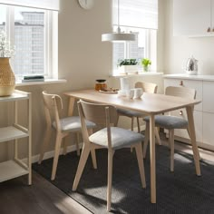 a dining room table with four chairs and a clock on the wall above it in front of a window